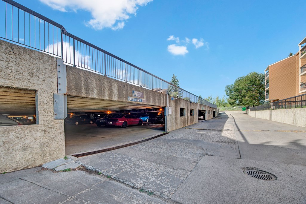 A concrete parking structure here at Gateway Square Apartment Homes under a clear blue sky. Several cars are visible inside, with a clearance sign above. An uphill driveway is on the right.