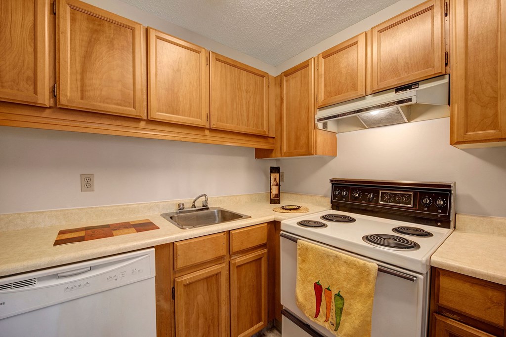 Cozy kitchen here at Gateway Square Apartment Homes with light wood cabinets, an electric stove, and beige countertops. A hand towel with chili peppers hangs on the oven, creating a warm, inviting feel.