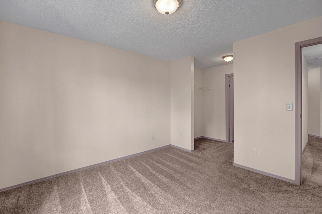 Empty bedroom here at Manning Crossing Apartment Homes with beige walls and carpet, featuring a small walk-in closet and simple ceiling light. The atmosphere is neutral and clean.