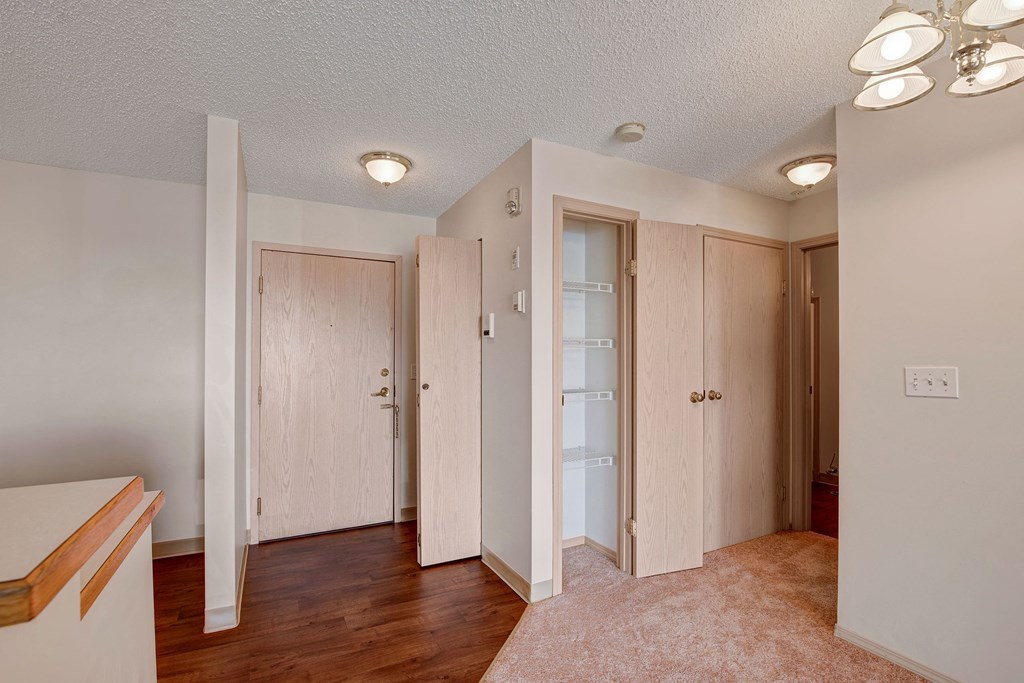 Simple room interior here at Manning Crossing Apartment Homes with beige walls, wooden doors, white closets, and mixed flooring. Three lights illuminate the space, creating a cozy atmosphere.