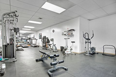 Gym interior here at Marquis Towers Apartment Homes with various exercise equipment, including treadmills, stationary bikes, and weight benches, in a clean, well-lit space with a white ceiling.