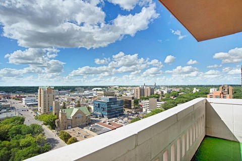 Aerial view of a cityscape from Marquis Towers Apartment Homes, featuring diverse buildings and a historic church. Fluffy clouds and a bright blue sky create a serene atmosphere.