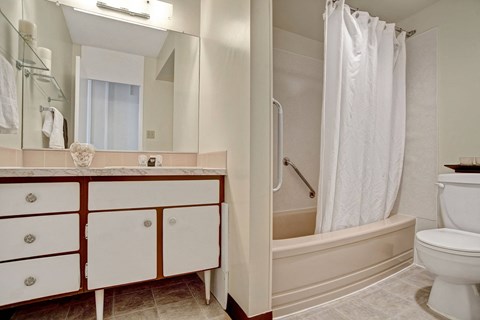 A clean bathroom here at Marquis Towers Apartment Homes with a cream bathtub and white shower curtain. A white toilet is nearby. The vanity features marble countertops and large mirrors, creating a fresh ambiance.