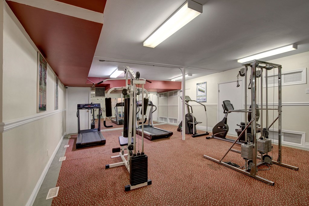 A small gym here at Park Place South Apartment Homes with carpeted floors and maroon ceiling. Contains exercise machines, including treadmills and a stationary bike, under bright fluorescent lights.
