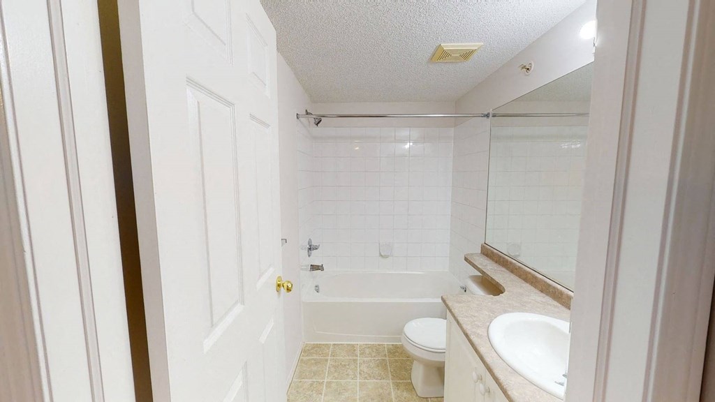 Bright bathroom here at The Pointe at Applewood with white tiles, a bathtub with shower, beige countertop with a sink, and a toilet. A serene and clean atmosphere.