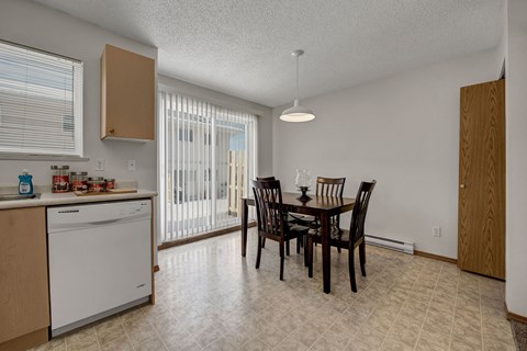 A bright dining area here at Ridgeview Village Apartment Homes with a dark wooden table and four chairs, set near large sliding glass doors with vertical blinds. A modern light fixture hangs above.