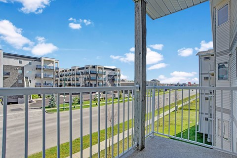 View from a balcony here at Windsor Terrace Apartment Homes showing a modern apartment complex across the street under a clear blue sky. The scene feels open and airy, with neatly trimmed grass.