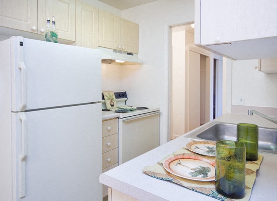 Bristol Square Kitchen A bright kitchen here at Bristol Square Apartment Homes with light wood cabinets, a white fridge, and a stove. Counter features two green glasses, plates with leaf designs, conveying a fresh, modern vibe.