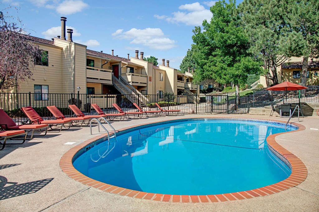 Grand View Pool Cozy apartment complex pool area here at Grand View Apartment Homes with red lounge chairs and umbrellas. Surrounded by trees and beige buildings under a clear blue sky. Calm and inviting.