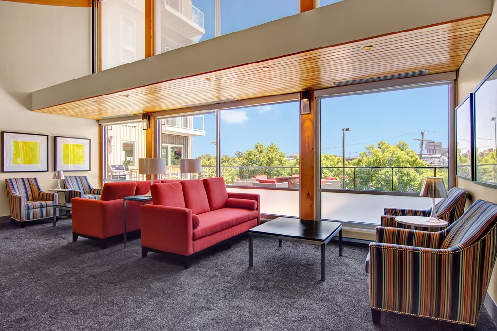 Spacious modern lounge here at 7west Apartment Homes with large windows, bright red couches, striped chairs, and abstract yellow art. Natural light creates a vibrant, welcoming atmosphere.