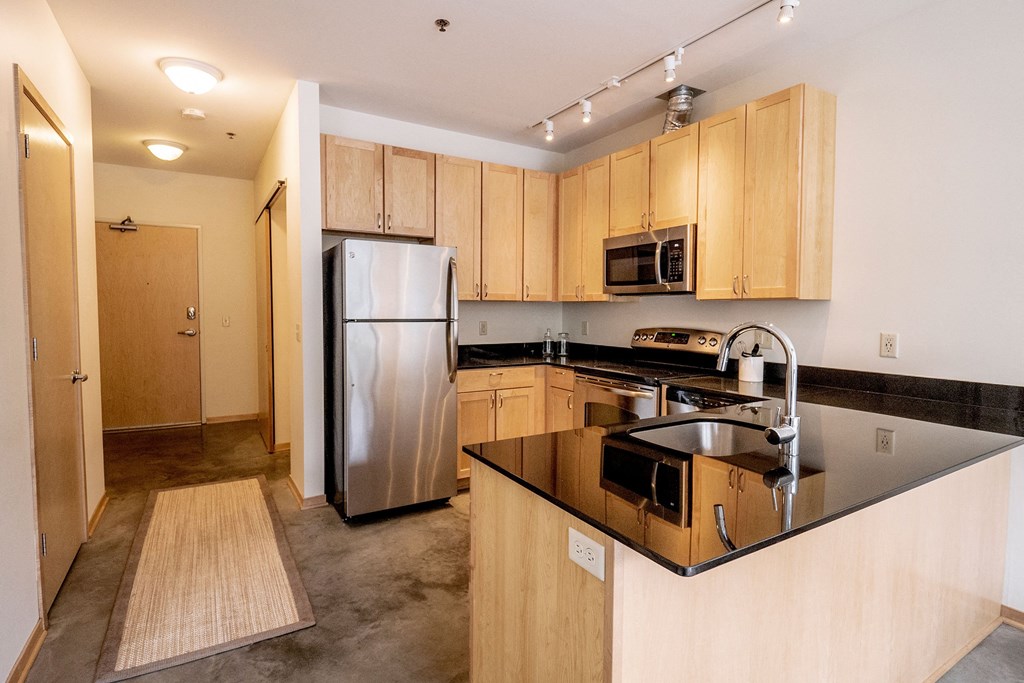 Modern kitchen here at 7west Apartment Homes with light wooden cabinets, stainless steel appliances, and a black granite countertop. It has a sleek, minimalistic design.