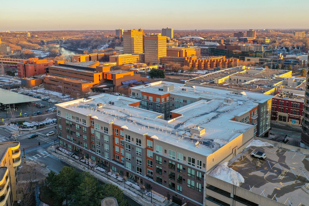 Aerial view of 7west Apartment Homes at sunset. Modern buildings with white and orange accents are prominent. Snow patches and trees are visible, conveying a calm winter scene.