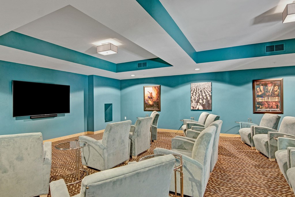 A cozy home theater here at The Covington Apartment Homes with teal walls features light gray recliner chairs, a large flat-screen TV, and framed movie posters, creating a relaxed ambiance.