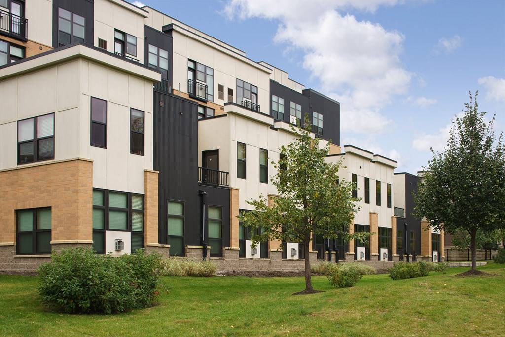 Modern townhouse complex here at Marbella on Dean Apartment Homes with a mix of brick and black siding, landscaped greenery, and clear blue sky creating a serene suburban atmosphere.