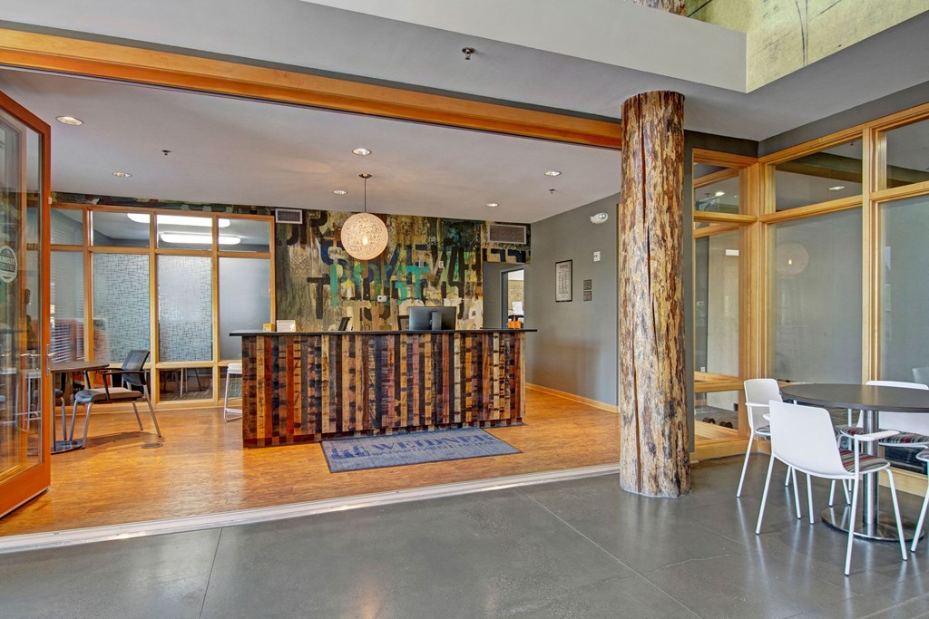 Contemporary office lobby here at Marbella on Dean Apartment Homes with a rustic wood reception desk, exposed log beams, and modern decor. Bright tone, open seating area, welcoming ambiance.