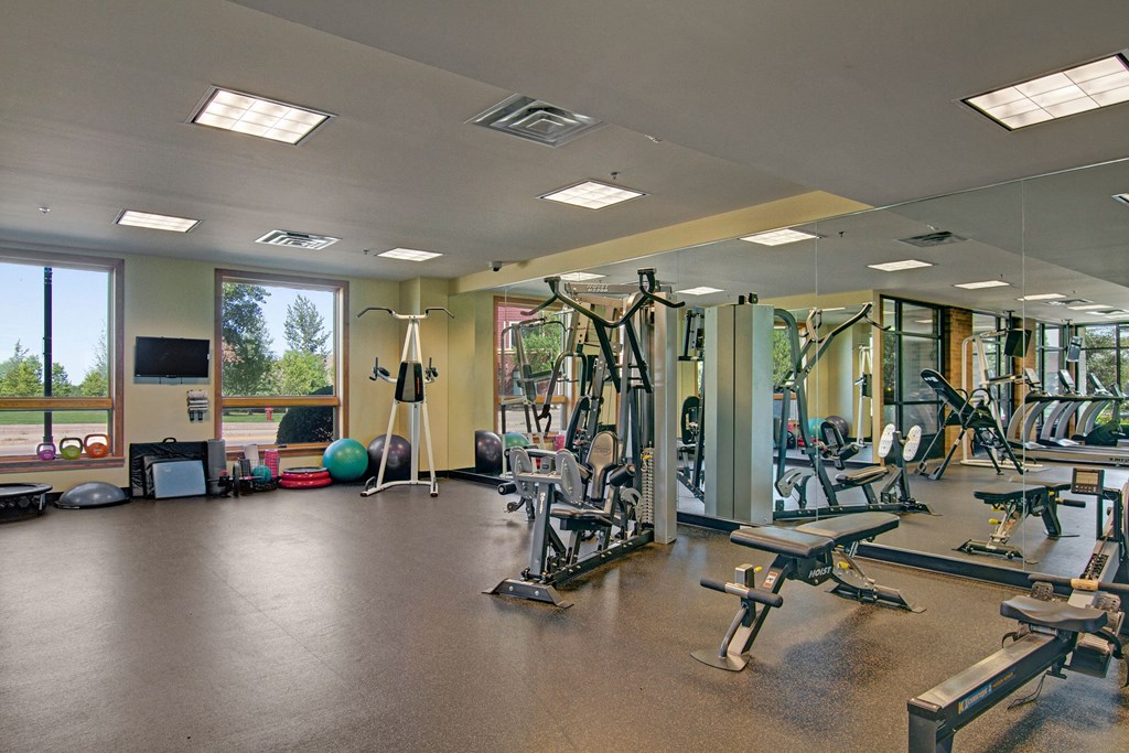 Spacious gym here at The Mist on Lake Minnetonka Apartment Homes with exercise machines, benches, and fitness balls. Large mirrors create an open feel. Bright daylight from windows, calm and focused ambiance.