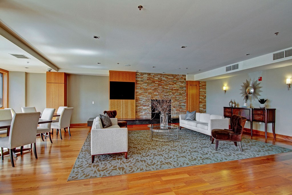 Spacious living room here at The Mist on Lake Minnetonka Apartment Homes with wooden floors and a patterned rug. Features beige sofas, a stone fireplace, and decorative wall mirrors, creating a cozy, elegant vibe.