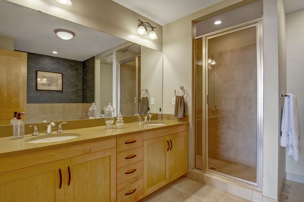 Modern bathroom here at The Mist on Lake Minnetonka Apartment Homes with wooden double vanity, large mirror, glass shower, and overhead lights. Neutral tones create a calm, clean atmosphere.