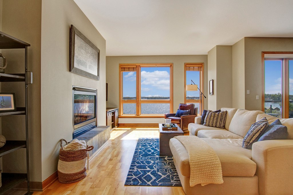 Spacious living room here at The Mist on Lake Minnetonka Apartment Homes with beige sectional sofa, blue patterned rug, and large windows showcasing lake views. Cozy ambiance with natural light.
