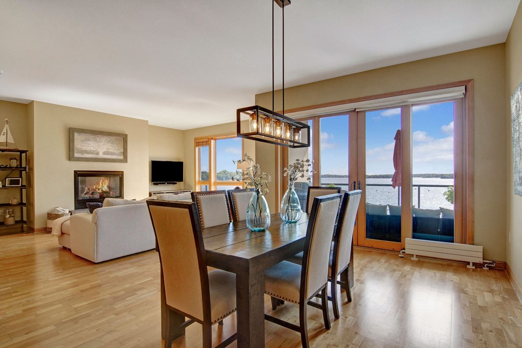 Bright living room here at The Mist on Lake Minnetonka Apartment Homes with wooden floors, featuring a dining table and chairs. Large windows showcase a scenic lake view. Cozy ambiance with soft lighting.