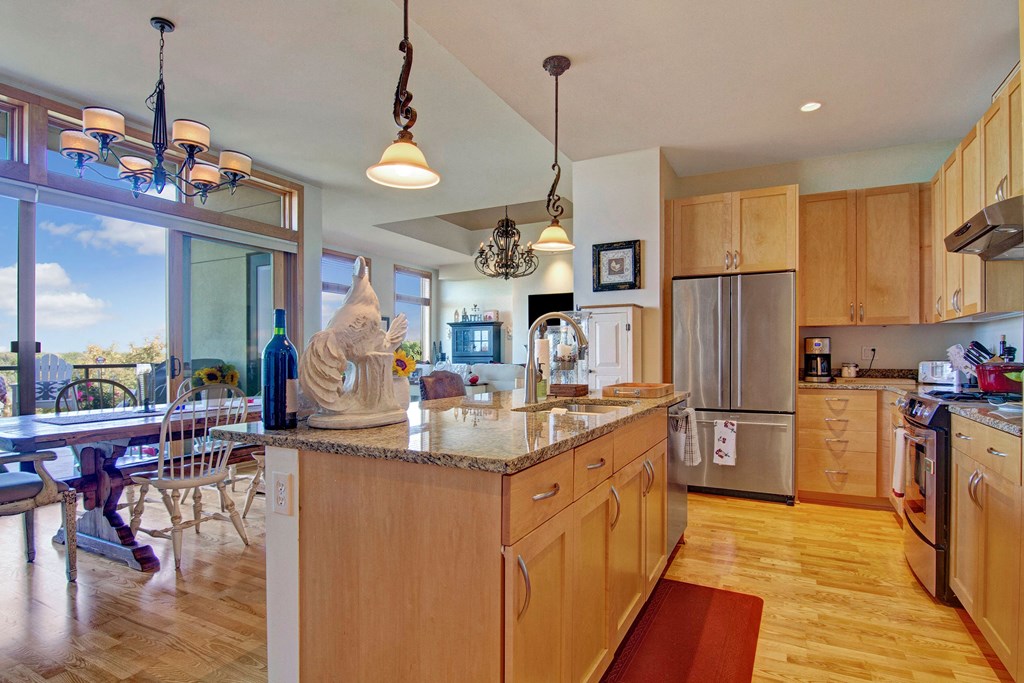 Bright kitchen here at The Mist on Lake Minnetonka Apartment Homes with wooden cabinets, granite island, and modern appliances. Dining area with large windows and decorative chandelier. Cozy, inviting feel.