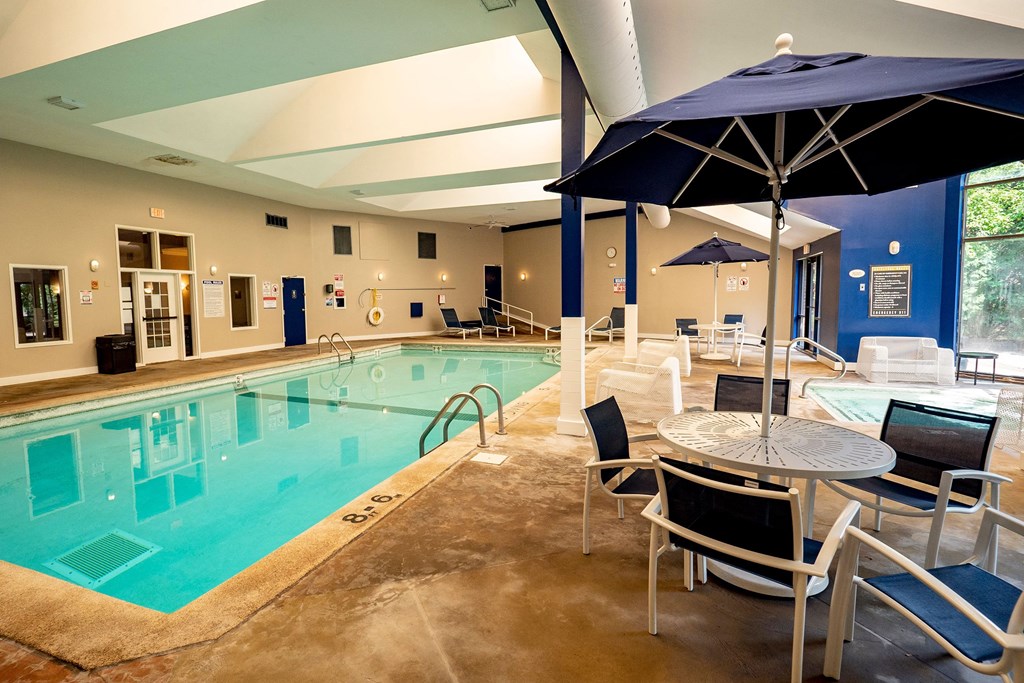Plymouth Square Pool Indoor pool area here at Plymouth Square Apartment Homes with calm water, lounge chairs, and tables with umbrellas. The setting is serene, featuring high ceilings and natural light.