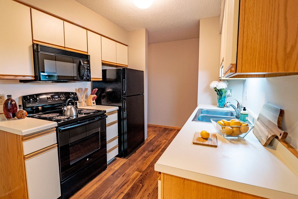 Plymouth Square Kitchen Bright kitchen here at Plymouth Square Apartment Homes with wood cabinets, black appliances, and white countertops. A bowl of lemons and flowers add freshness. Cozy, welcoming vibe.