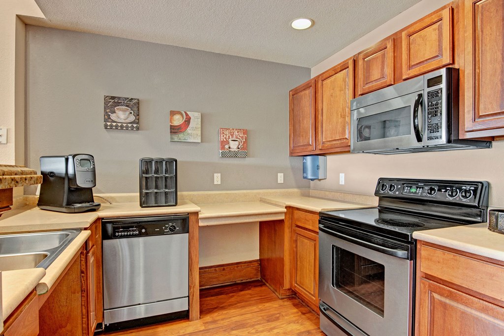 Warm-toned kitchen here at Stoneleigh at The Reserve Apartment Homes with wooden cabinets, stainless steel appliances, and coffee-themed wall art. Cozy, organized, and modern interior design.