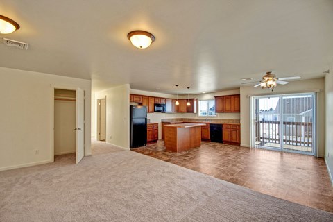 Spacious open-plan living area here at Phoenix Ridge Apartment Homes with beige carpet and tiled kitchen. Features wooden cabinets, center island, glass doors to balcony, and a cozy, bright ambiance.