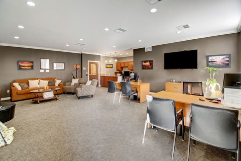 Modern office lounge here at Prairie Pines Apartment Homes with a warm, inviting atmosphere. Features a brown sofa, patterned chairs, wooden desks, computer stations, and abstract art.