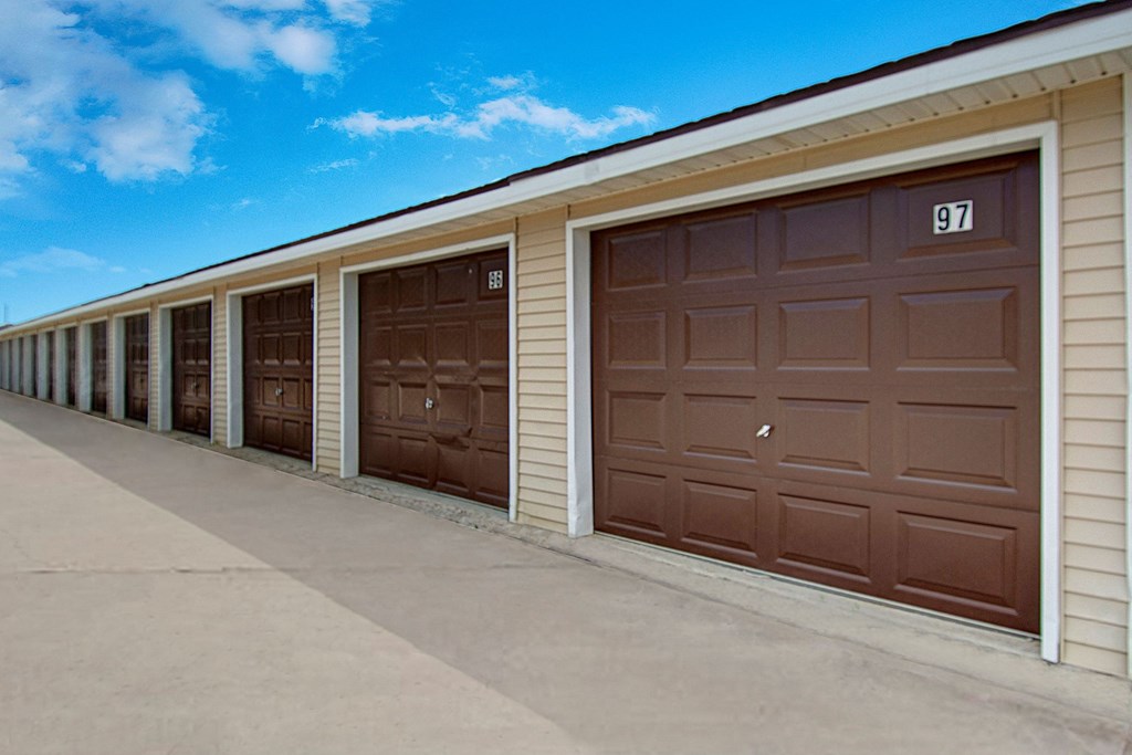 A row of storage unit garages here at Windscape Apartment Homes with brown doors and numbered labels under a clear blue sky. The scene conveys a sense of order and functionality.