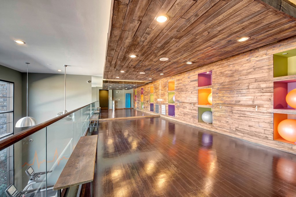Stylish studio with polished floors here at the Enclave at Brookside Apartments, rustic wooden ceiling, colorful walls and recessed cubbies holding exercise balls, creating a vibrant, airy atmosphere.