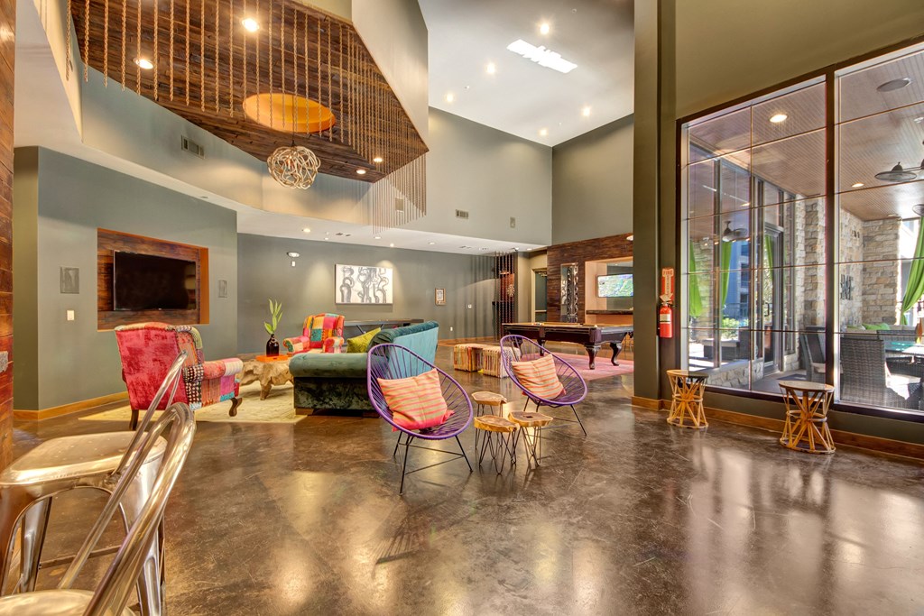 Spacious modern lounge here at the Enclave at Brookside Apartments with colorful furniture and high ceilings, featuring a pool table, wall art, and bright lighting for a lively, inviting atmosphere.