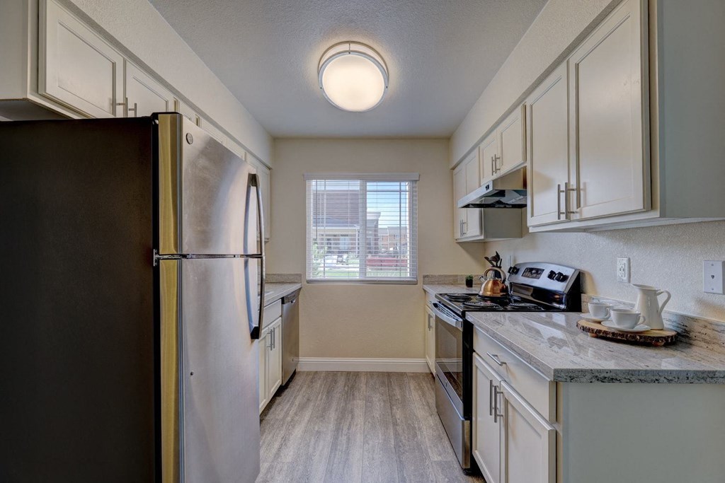 Indigo Apartments Kitchen Modern kitchen here at Indigo Apartment Homes with stainless steel appliances, white cabinets, and marble countertops. A window with blinds reveals a sunny day outside.