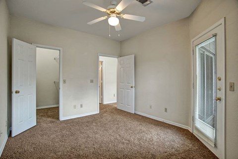 Lincoln Villas on Memorial Bedroom Empty room here at Lincoln Villas on Memorial Apartment Homes with beige walls and brown carpet, featuring two open white doors, a ceiling fan with a light, and a glass door with blinds.