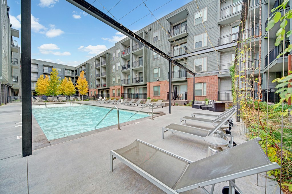 Modern courtyard here at The Metropolitan Apartment Homes with a swimming pool, surrounded by four-story buildings. Lounge chairs line the poolside, with autumn trees adding color.
