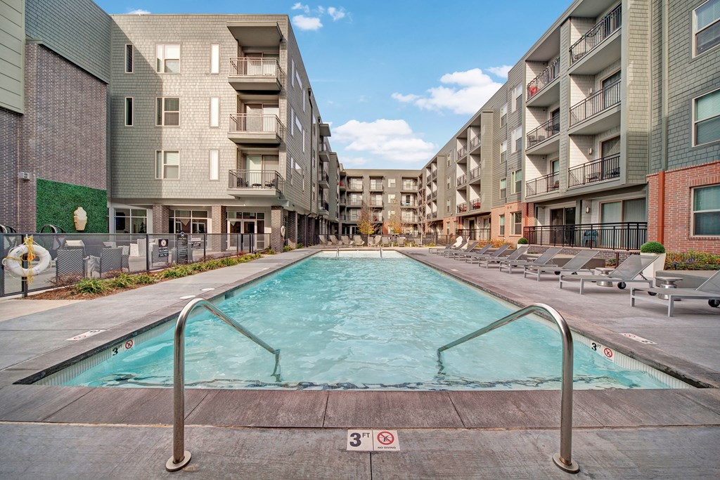 Modern The Metropolitan Apartment Homes with a central rectangular pool surrounded by lounge chairs. The buildings are four stories high, and the setting is calm and inviting.
