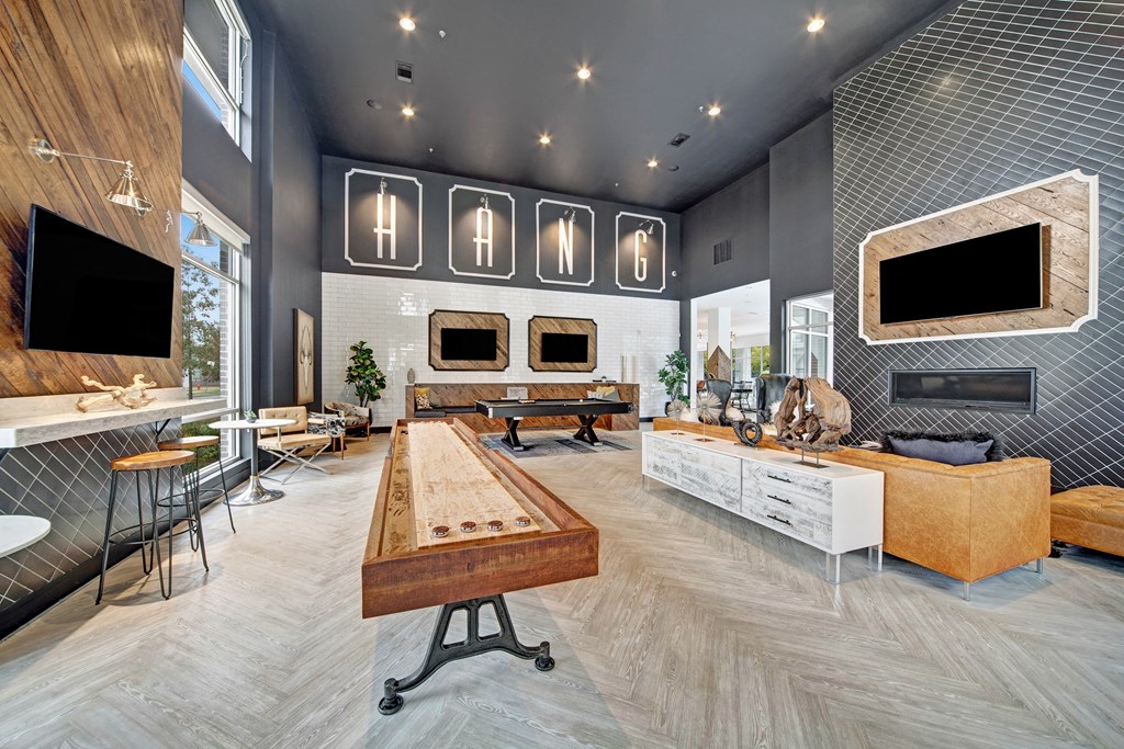 Modern lounge here at The Metropolitan Apartment Homes with tall ceilings, featuring leather seating, wall-mounted TVs, and a foosball table. Bright, inviting, and stylish decor.