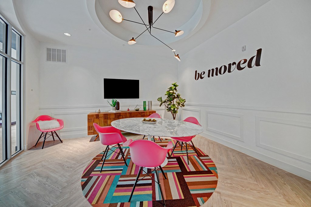 Modern conference room here at The Metropolitan Apartment Homes with a round marble table, pink chairs, and a bold art piece reading "be moved." Bright, inviting atmosphere with sleek decor.