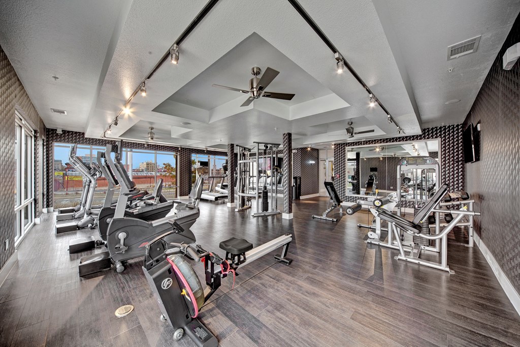 Modern gym here at The Metropolitan Apartment Homes with large windows, featuring treadmills, a rowing machine, and various weight machines. Bright, airy, with a sleek and clean design.
