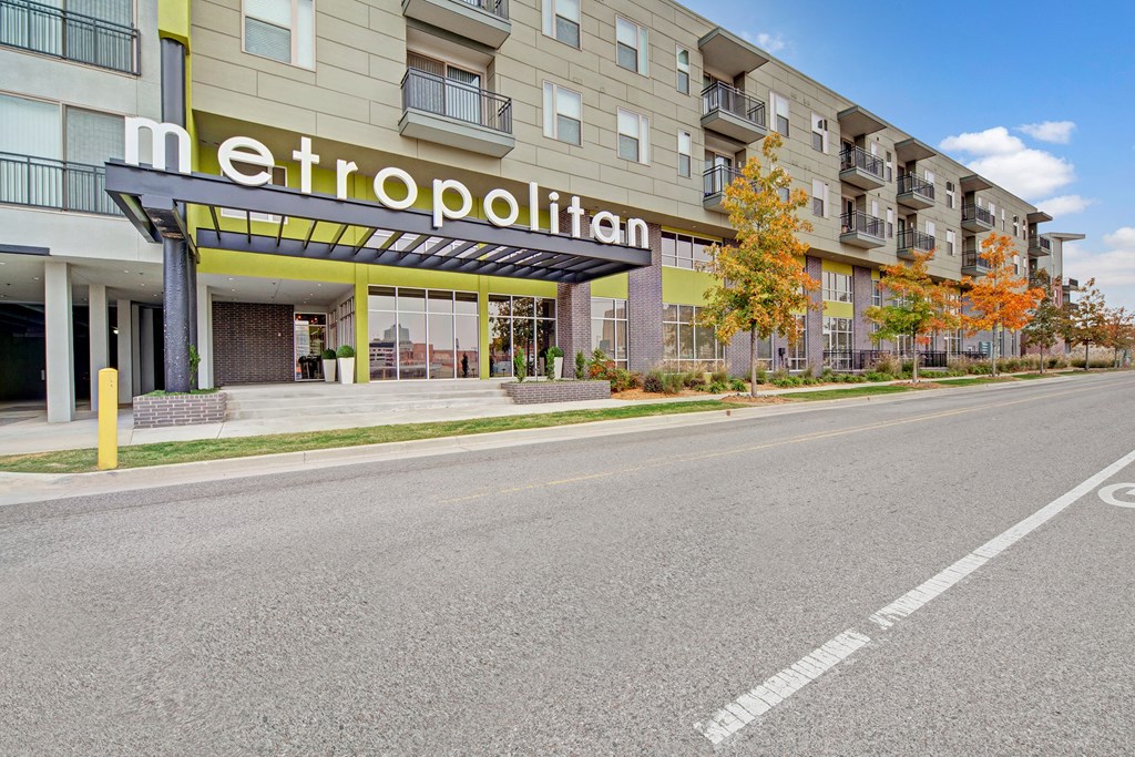 A modern apartment building labeled "Metropolitan" features a spacious entrance, autumn trees, and a clear sky, conveying a welcoming urban atmosphere.