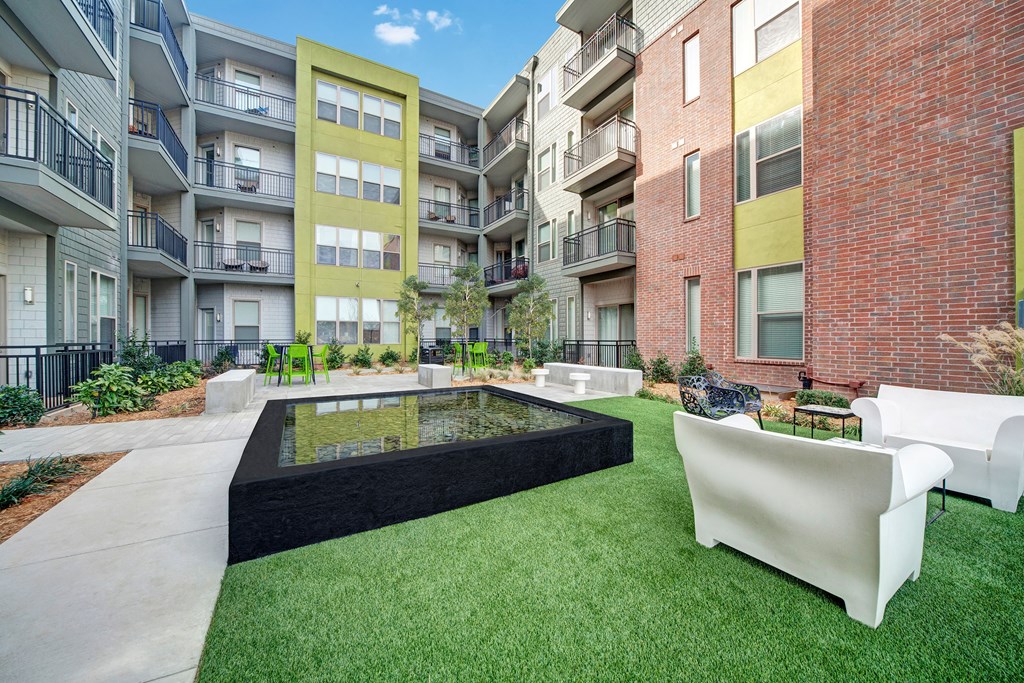 Modern courtyard here at The Metropolitan Apartment Homes features a reflective water fountain, surrounded by green artificial grass, outdoor seating, and multi-level balconies.
