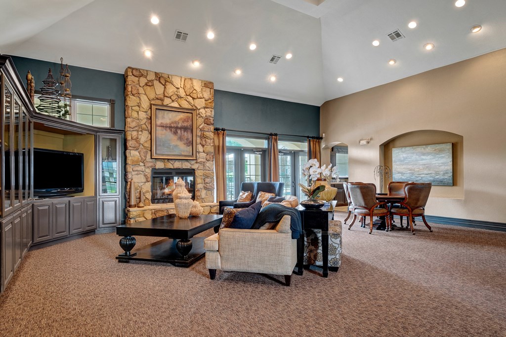 Spacious lounge here at Quail Landing Apartment Homes with high ceiling, stone fireplace, and modern decor. Comfortable seating surrounds a dark coffee table, evoking a cozy, elegant vibe.