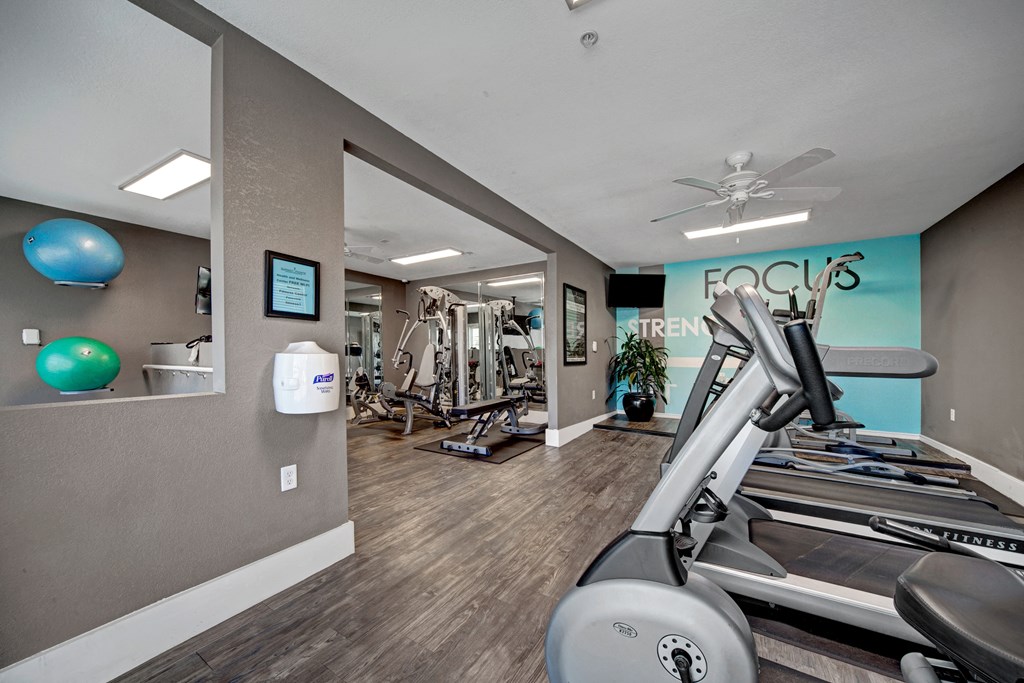 Modern gym interior here at Summit Point Apartment Homes with treadmills, weight machines, and exercise balls. A bright turquoise accent wall with "Focus Strength" adds vibrancy.
