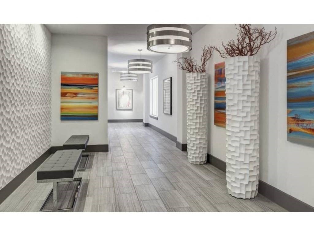 Modern hallway here at Arpeggio Apartment Homes with textured white walls and gray tile floor. Features abstract art, two tall white vases with branches, and sleek benches, creating a stylish, contemporary vibe.