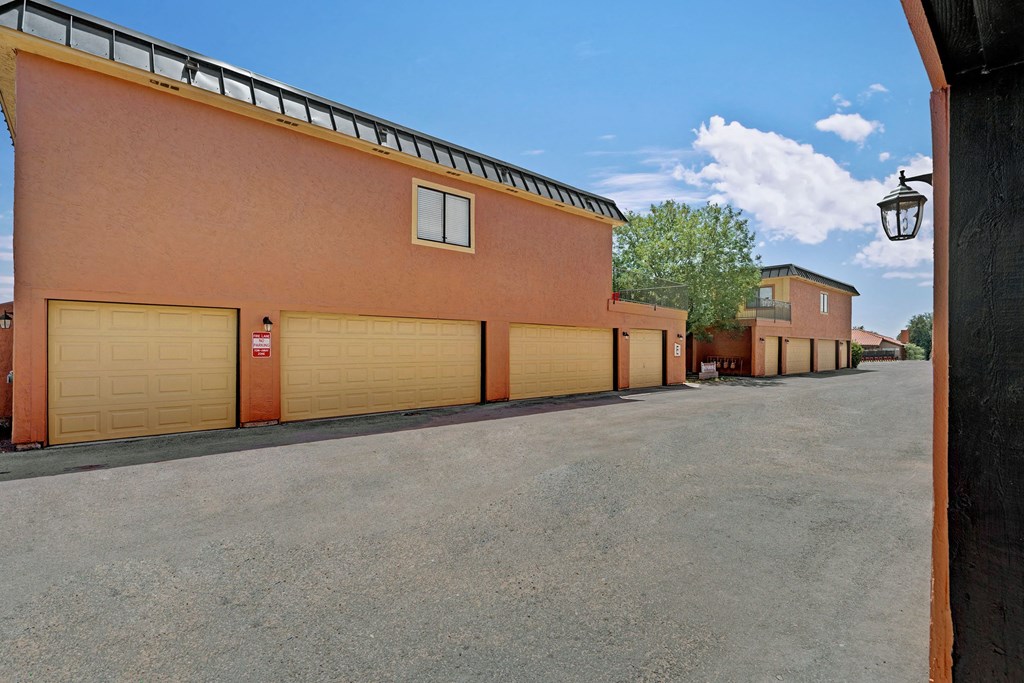 A row of peach-toned garages here at Avanti Townhomes with yellow doors under a clear blue sky. There are trees and two-story buildings, creating a serene, residential atmosphere.
