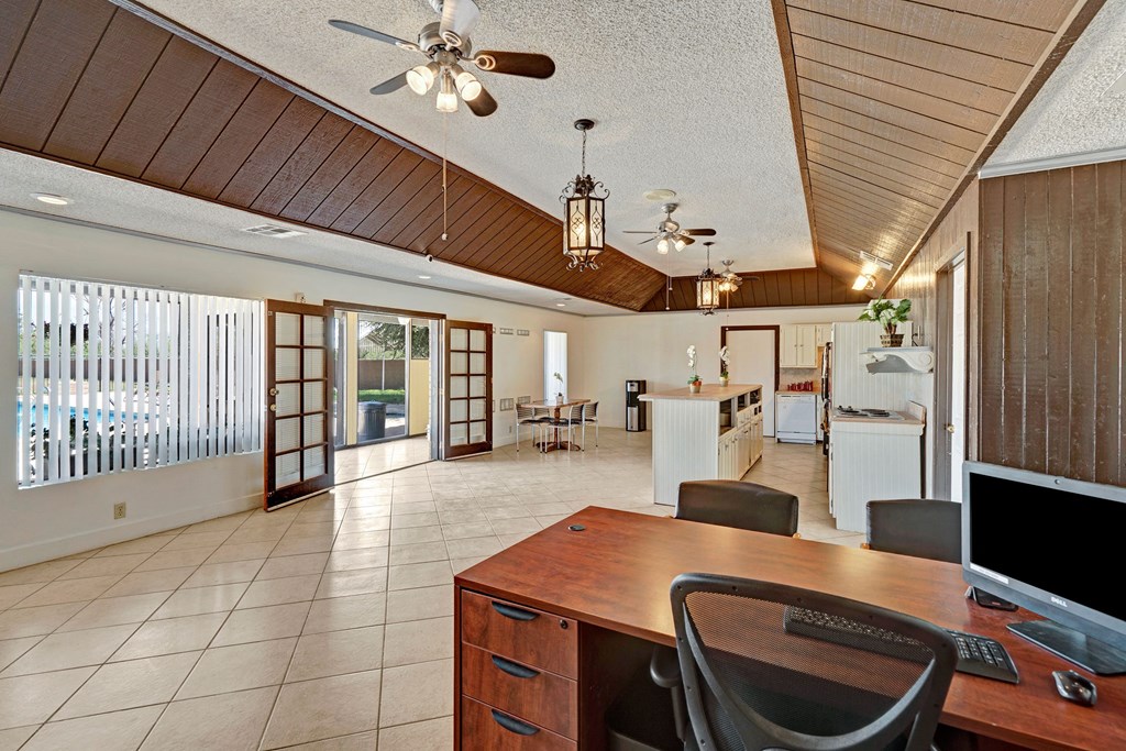 Spacious office here at Avanti Townhomes with wooden furniture, ceiling fans, and large windows facing a pool. Neutral tones create a bright, welcoming atmosphere.