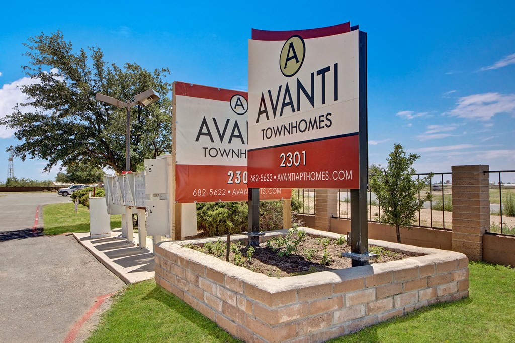 Sign for Avanti Townhomes with contact details, set against a blue sky. Nearby are mailboxes and a tree, conveying a suburban feel.