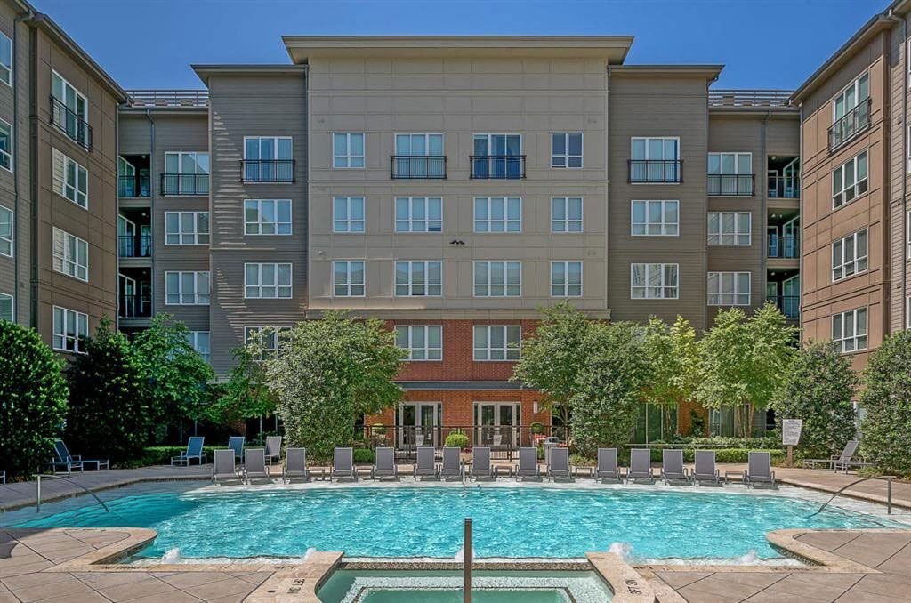 Modern Cityplace Heights Apartment Homes complex with a central swimming pool lined with lounge chairs. Surrounding greenery adds a refreshing touch under the clear blue sky.