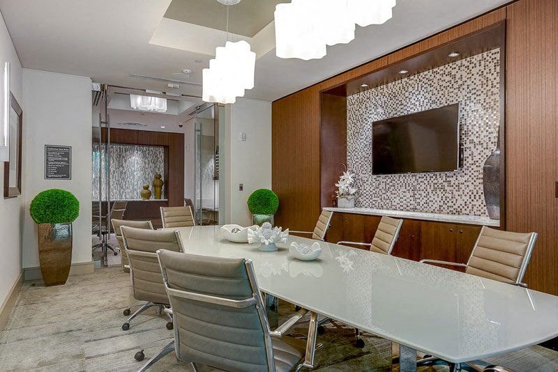 Sleek conference room here at Cityplace Heights Apartment Homes with a long white table, beige chairs, mosaic wall with a flat-screen TV, modern lights, and decorative greenery.